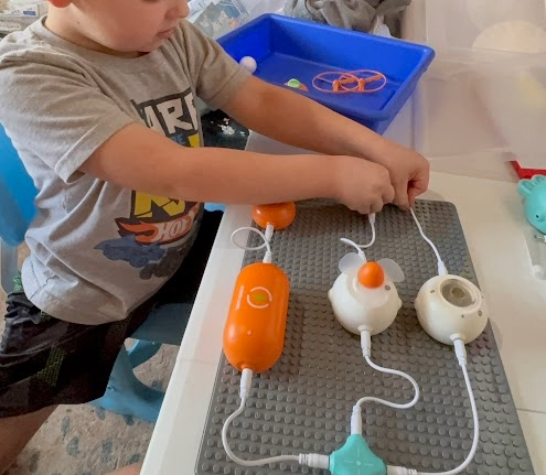 A child playing with educational toy appliances connected with wires on a table.