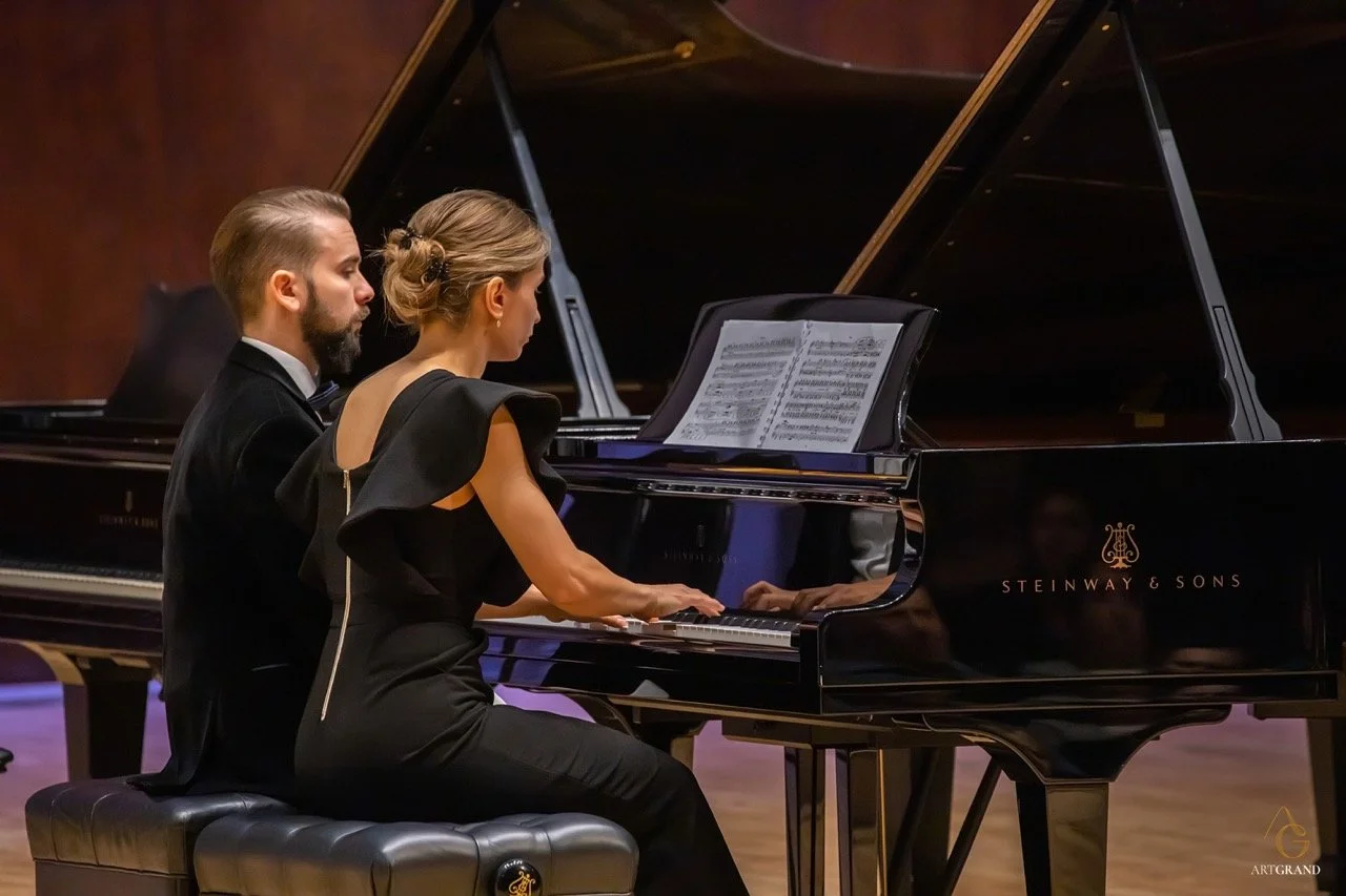 Two adult pianists performing together at a Steinway & Sons grand piano during an advanced classical piano performance