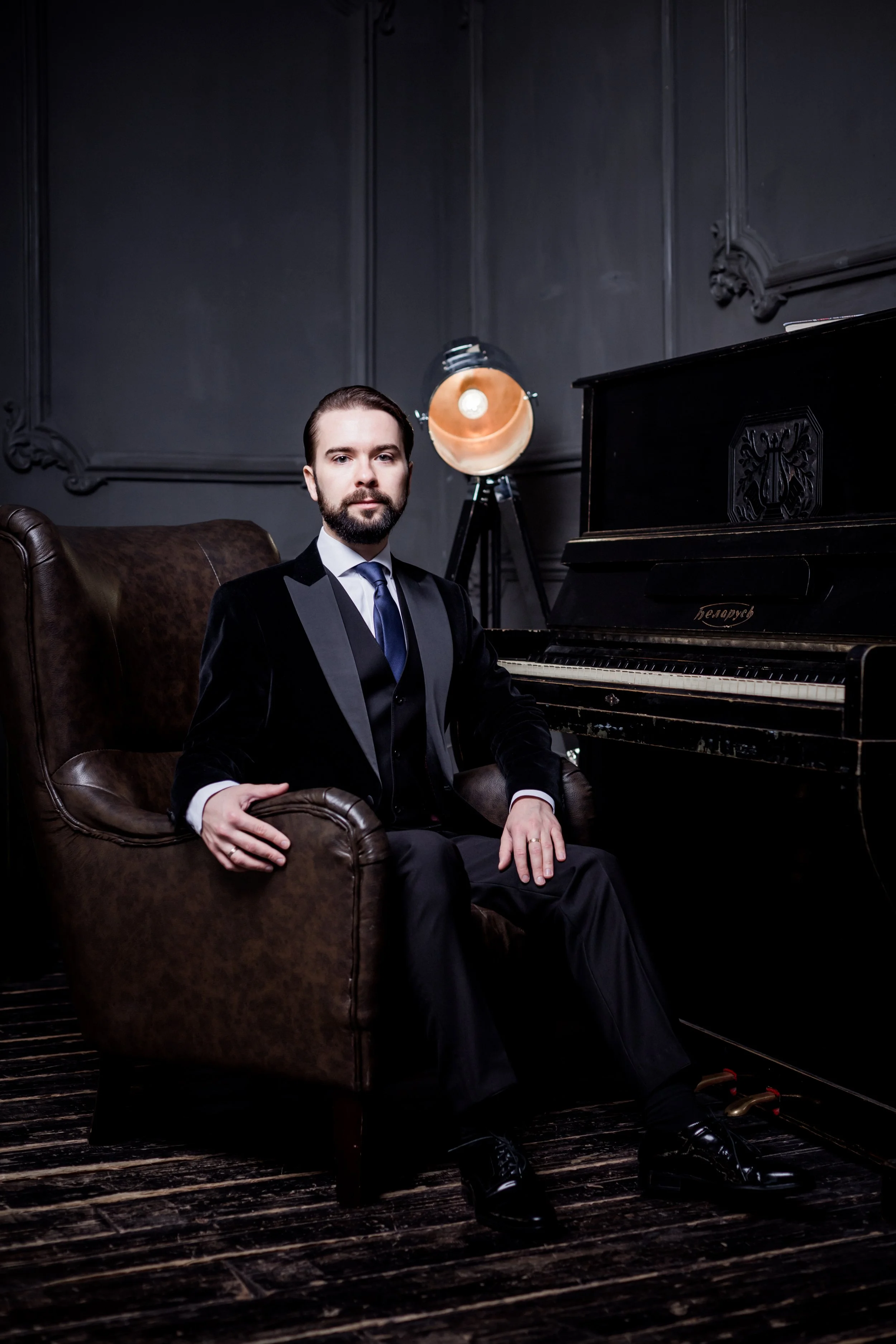 Artiom Shaplyka, concert pianist, piano educator, and founder of Miami Beach Piano Studio, seated beside a piano in a formal portrait