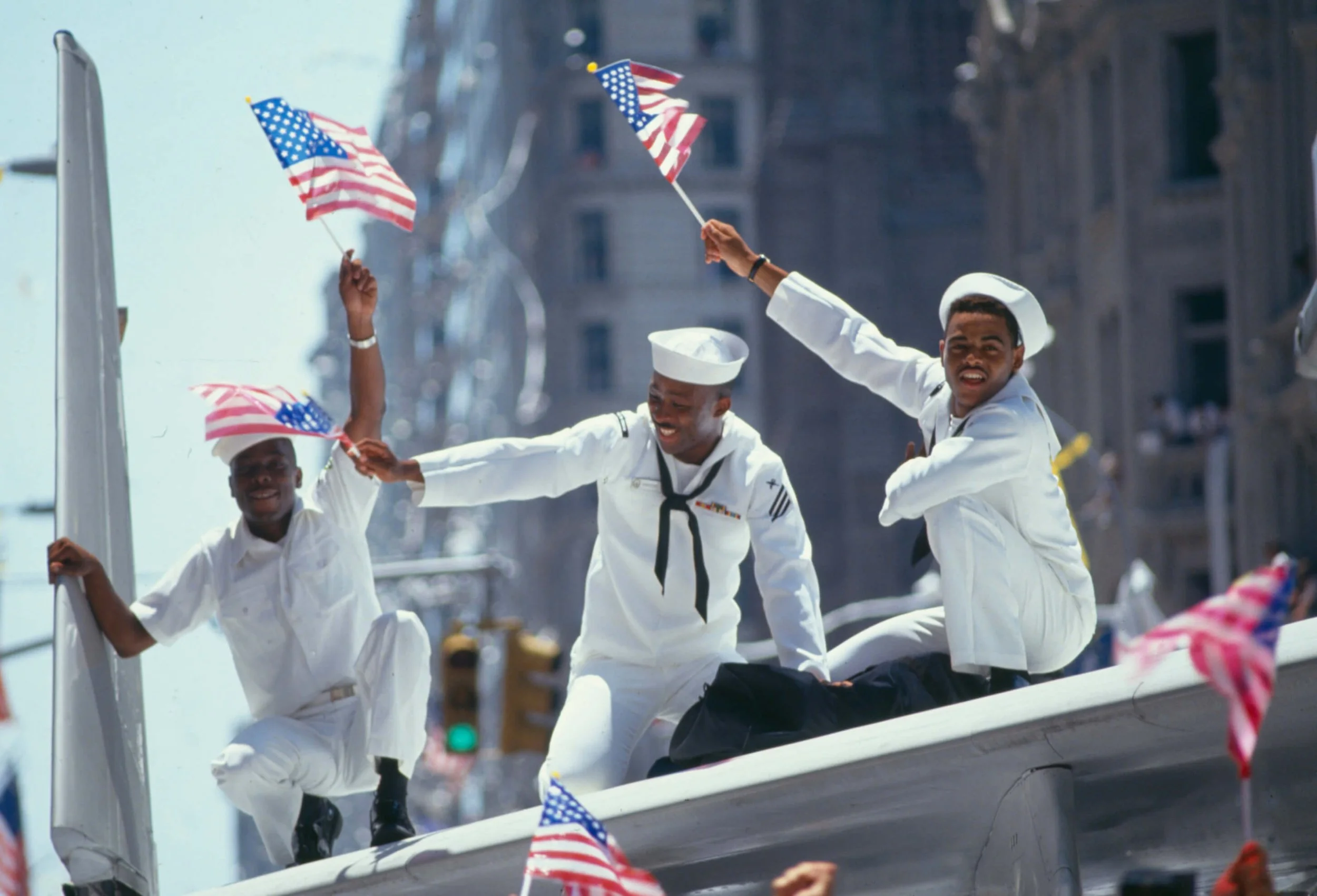 People dressed in navy uniforms celebrating on a parade float decorated with American flags.