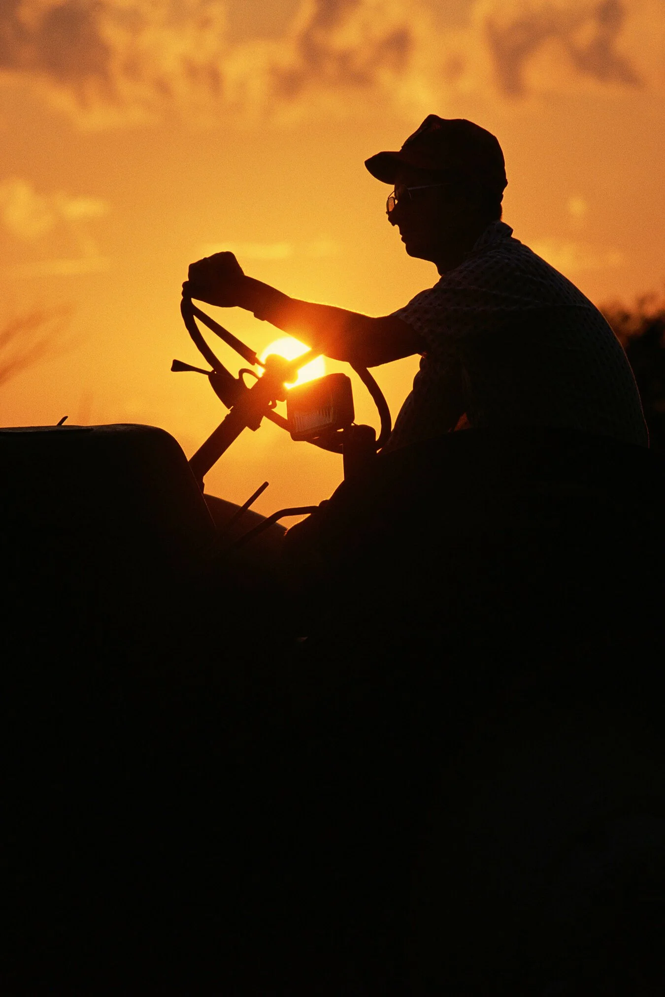 Silhouette of a person riding a tractor at sunset.