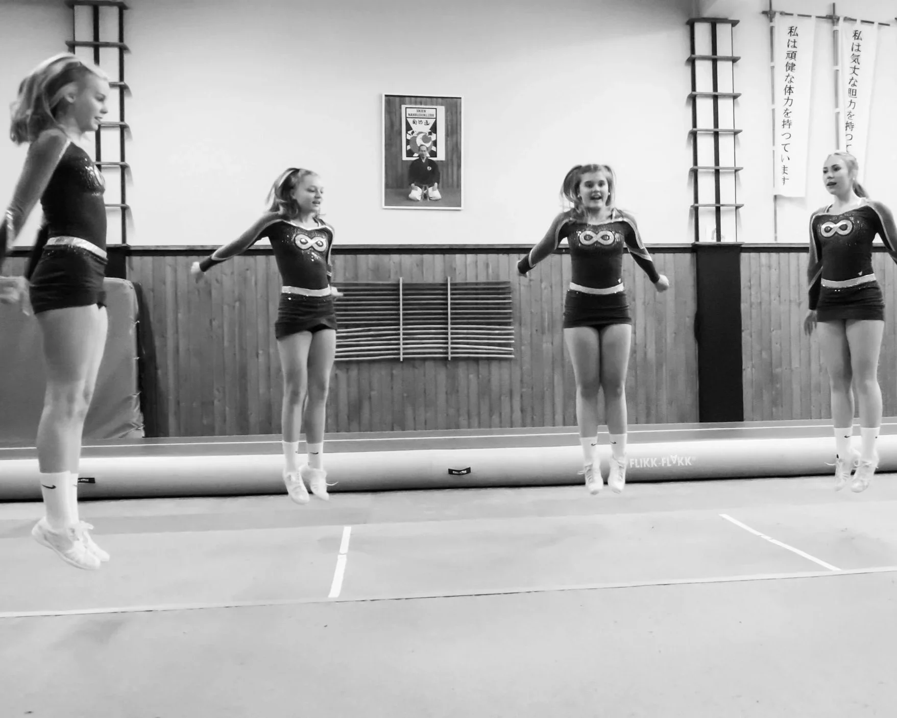 Two women exercising with battle ropes in a gym, one woman in the foreground and one in the background, on a green turf floor.