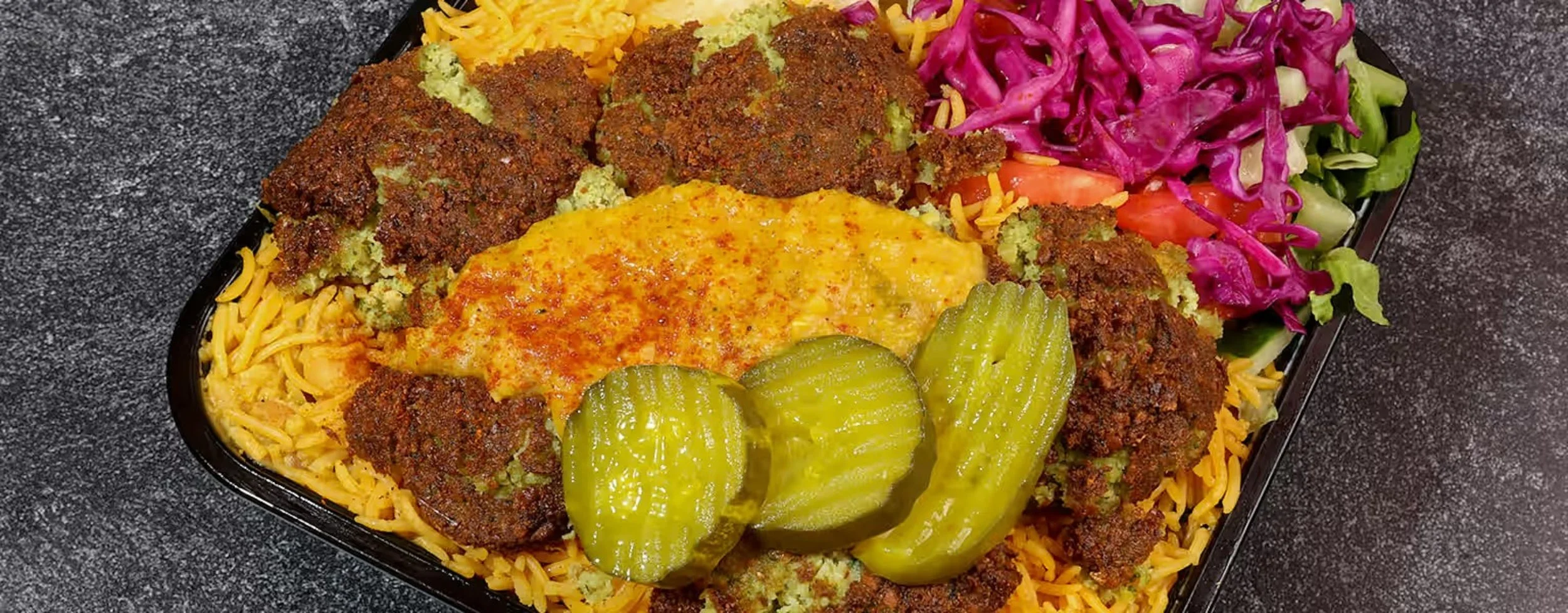 A takeout tray with yellow rice topped with our falafel platter.