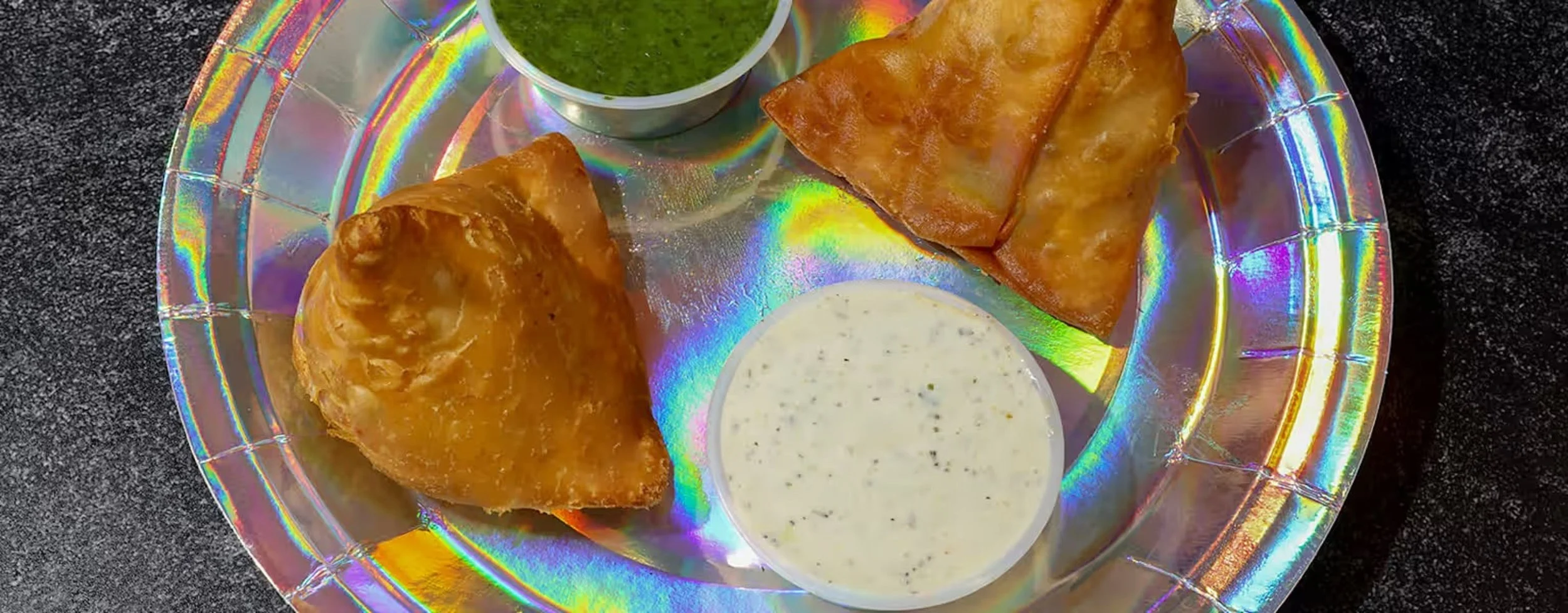 Plate with two samosas, two slices of stuffed bread, green chutney, and white dipping sauce.