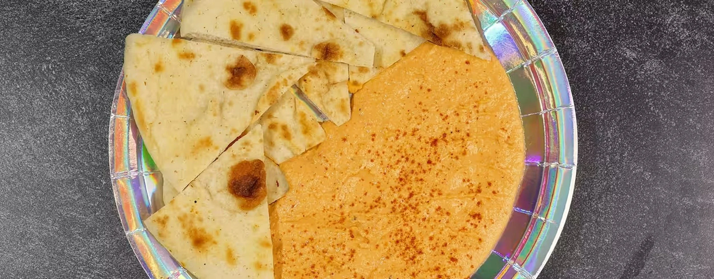 A plate with sliced pitta bread and a large portion of dip on a black countertop.