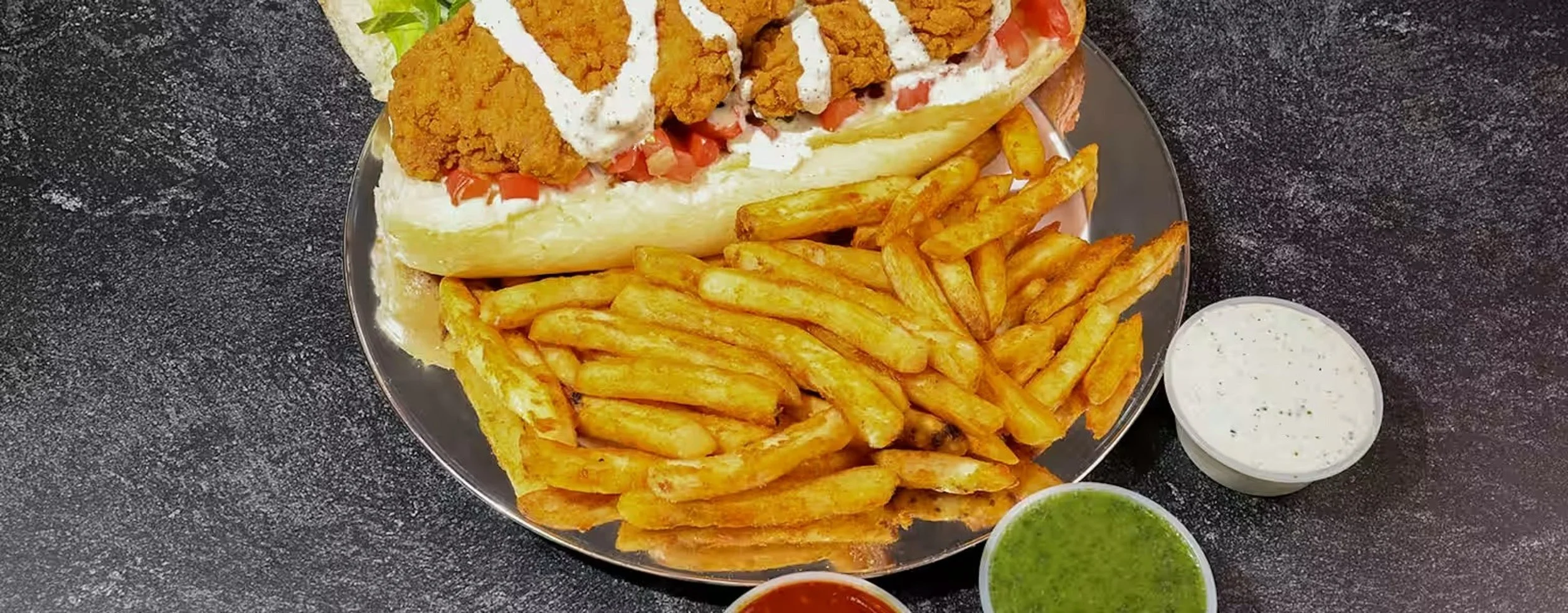 Plate of fried chicken sandwich with fries and three dipping sauces.
