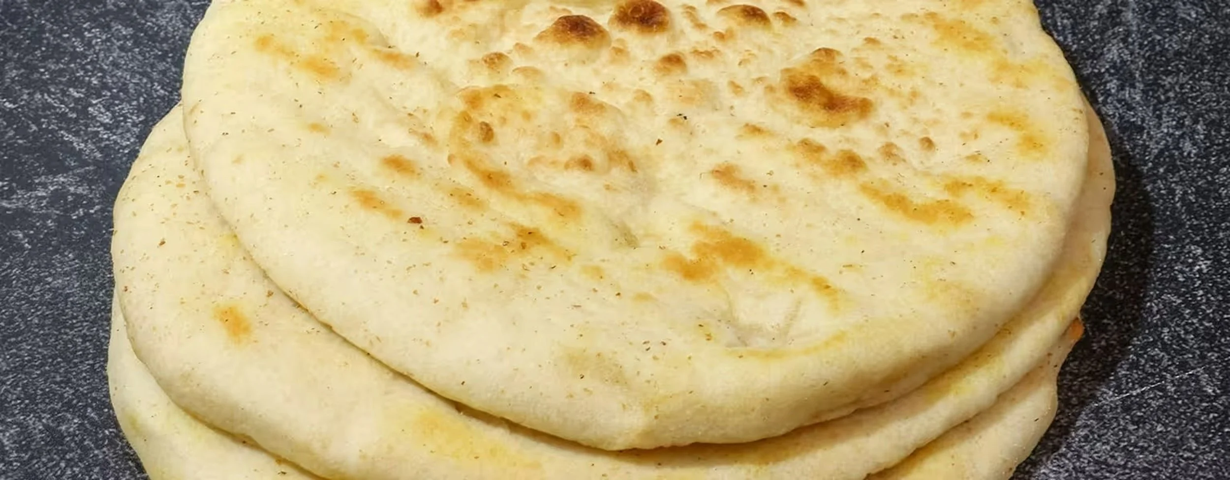 Three pieces of flatbread or naan stacked on a dark speckled surface.