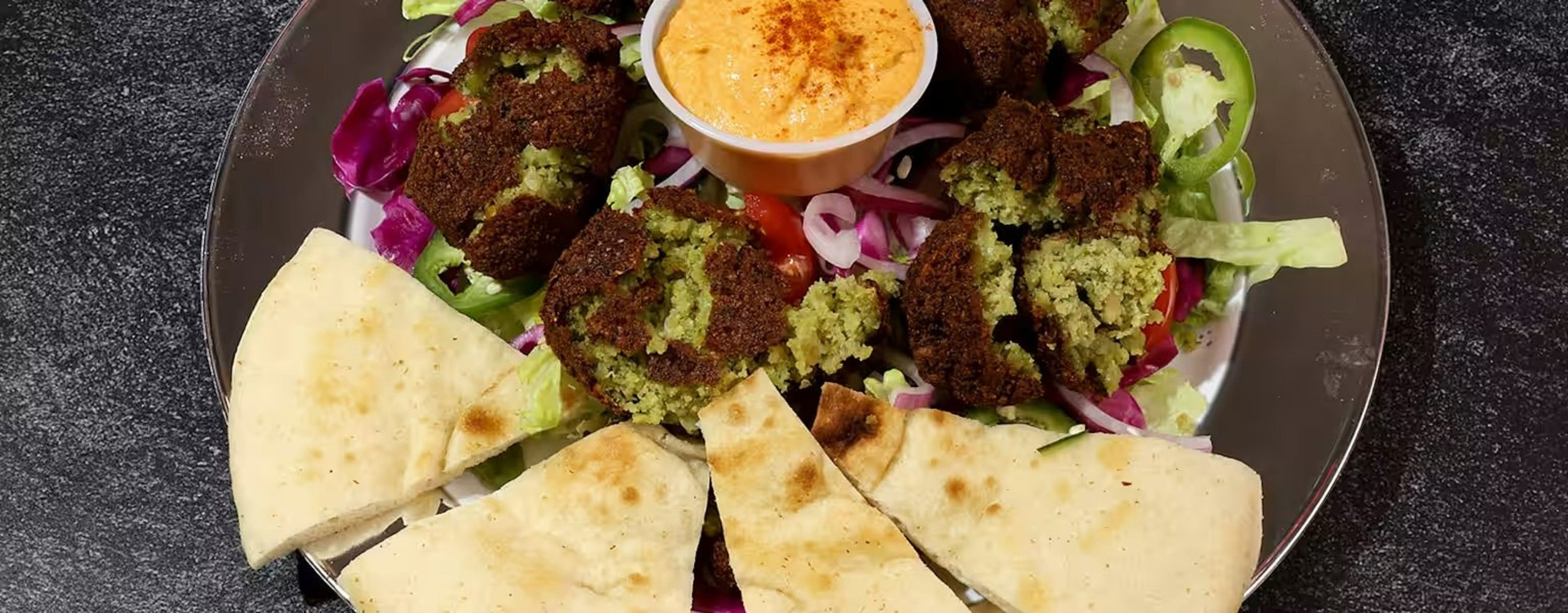 A plate of falafel with pita bread, fresh vegetables, and a side of dipping sauce.