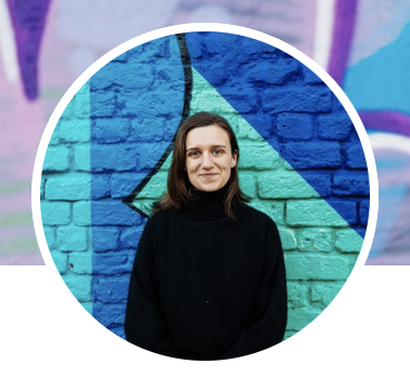 Portrait of women with shoulder length hair, wearing a black, in front of a brick wall painted in blue.
