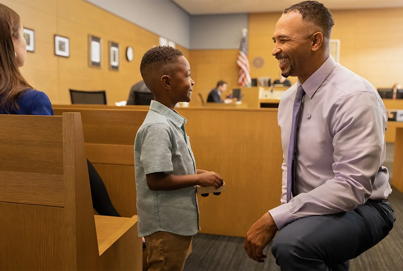 A courtroom scene featuring a man and young boy smiling, representing a CASA volunteer advocating for a child.