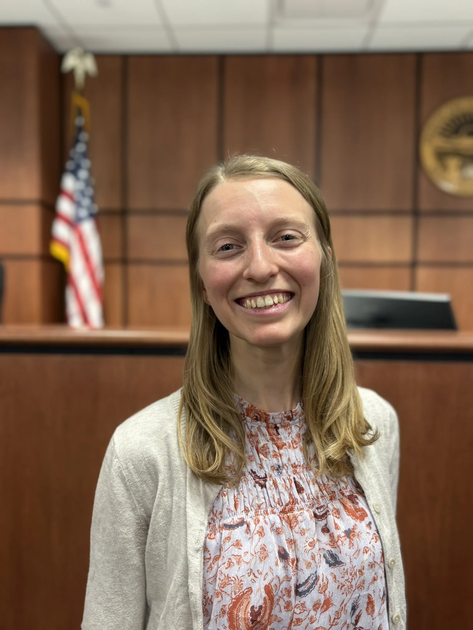 A smiling woman standing in a courtroom. This is Erin Grohe, the Program Director of CASA of Medina County.