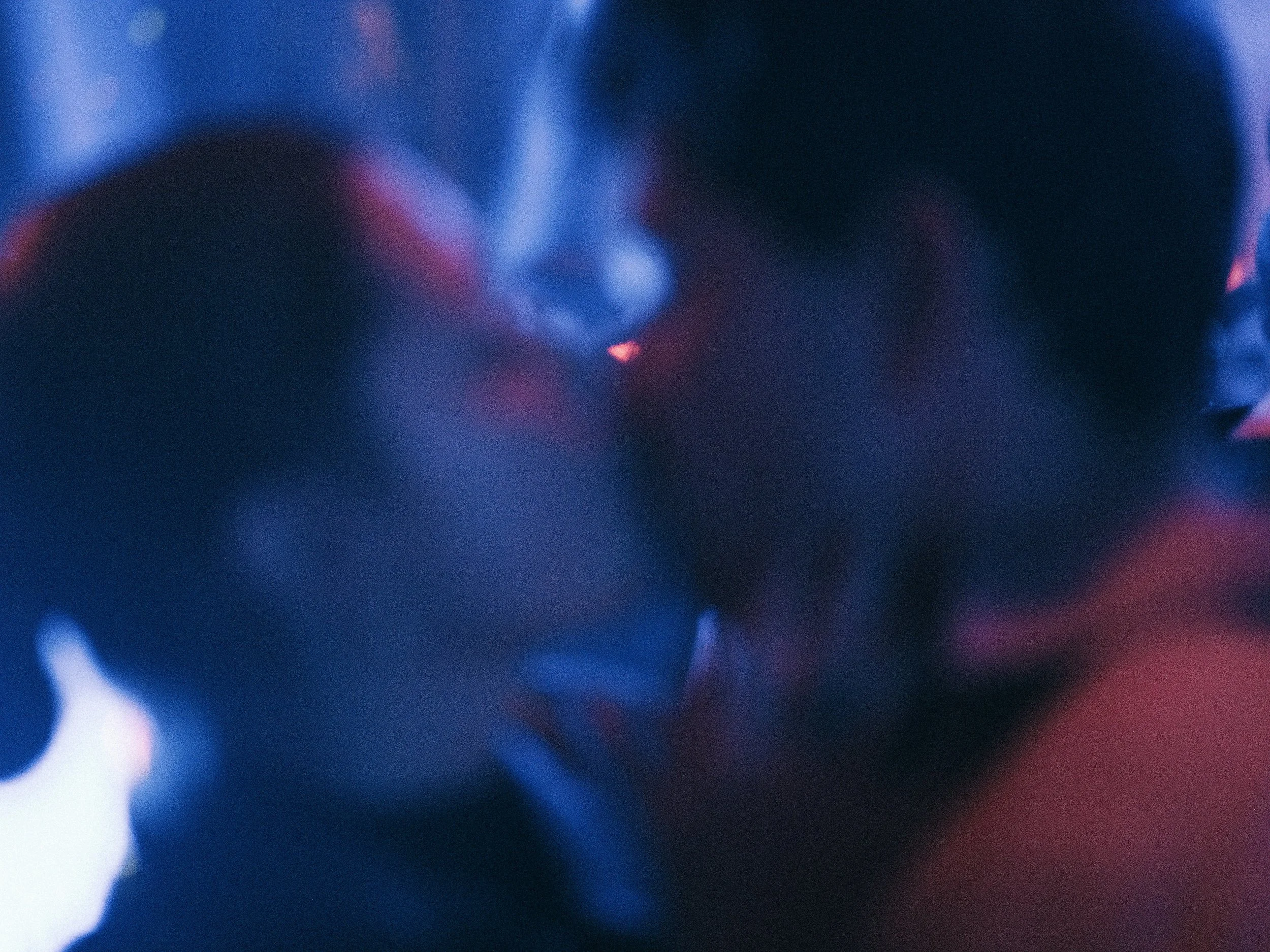 Close-up image with dark tones and red and blue lighting, showing abstract faces or figures.