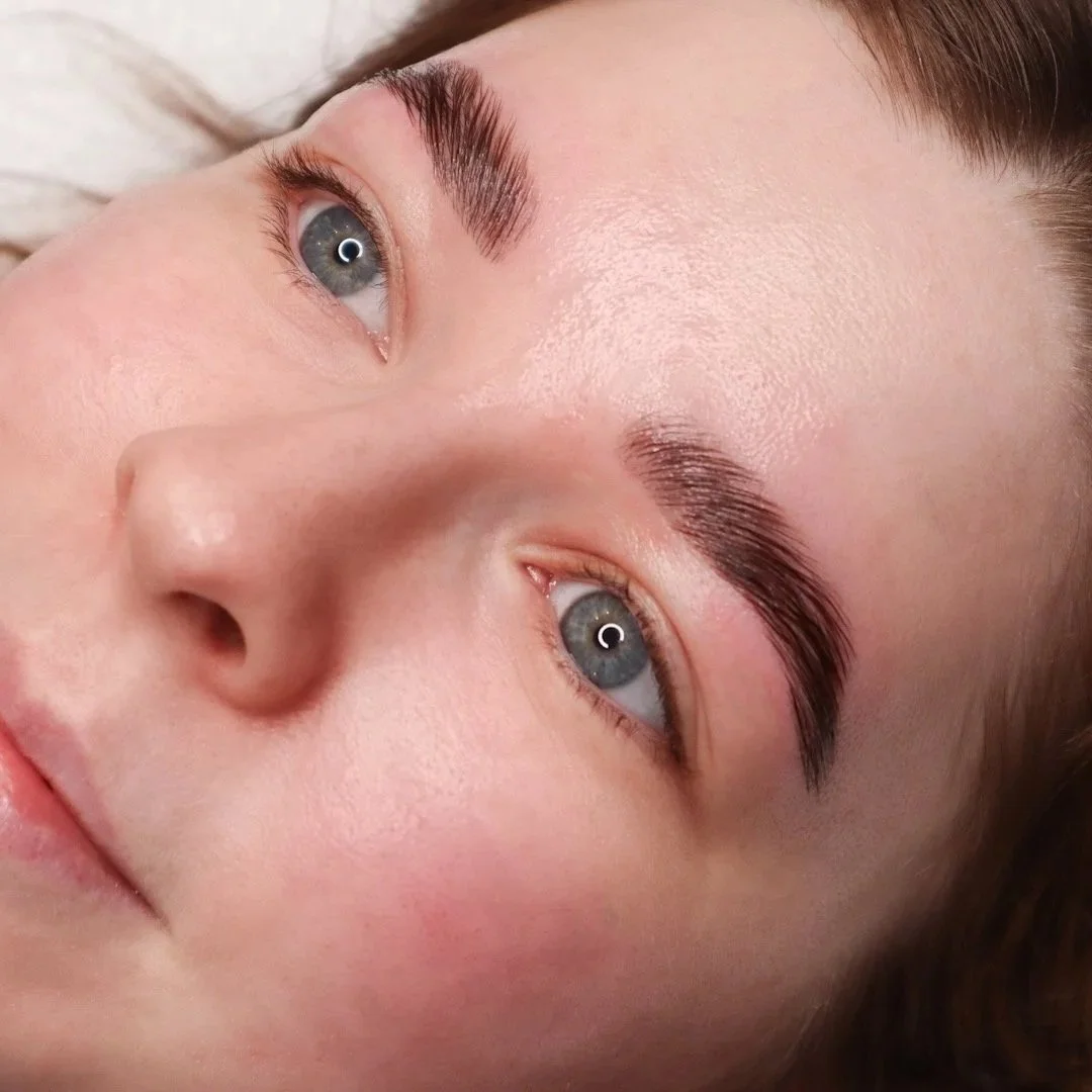 Close-up of a woman's face lying down, showing her eyes, nose, and part of her lips. She has blue eyes, well-groomed eyebrows, and clear skin.