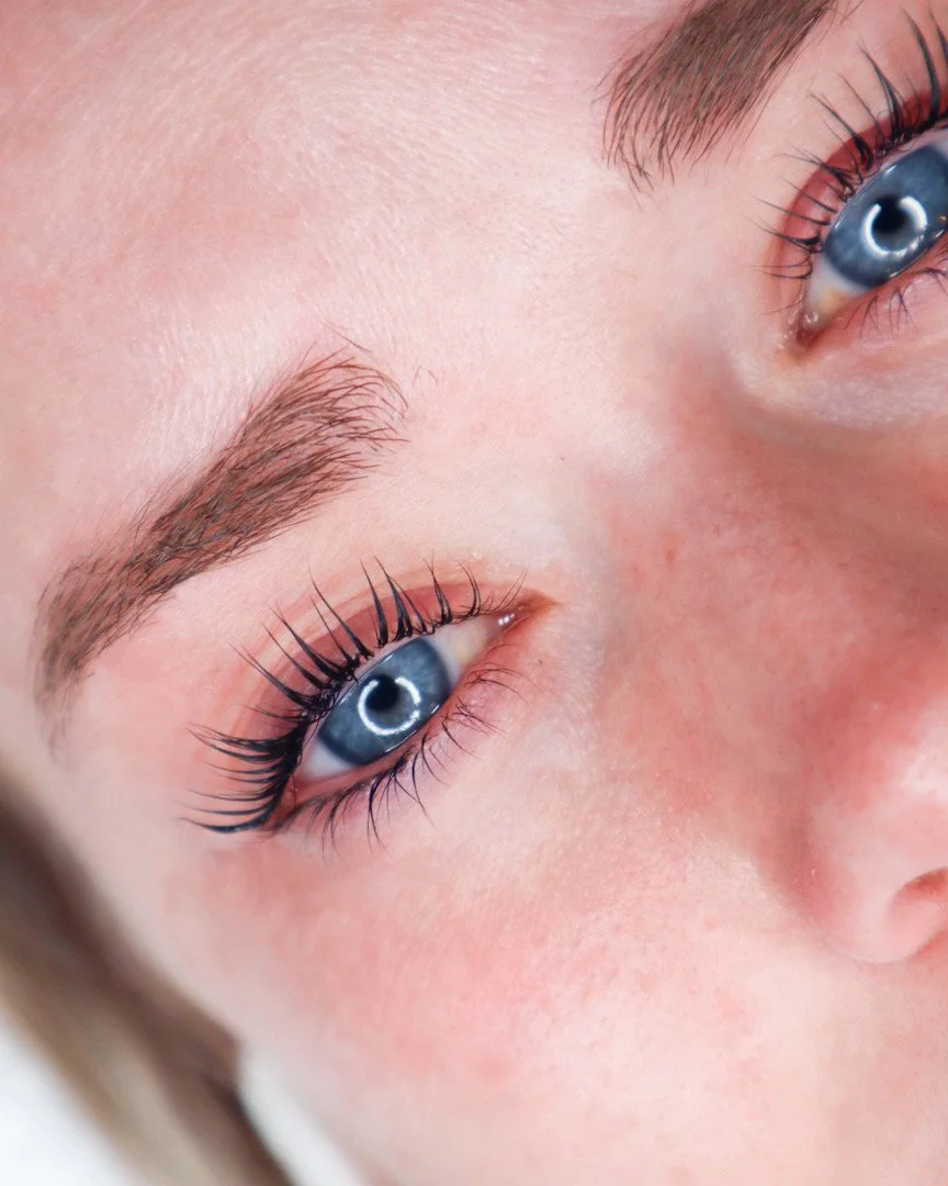 Close-up of a person's face showing blue eyes, well-groomed eyebrows, and long eyelashes.