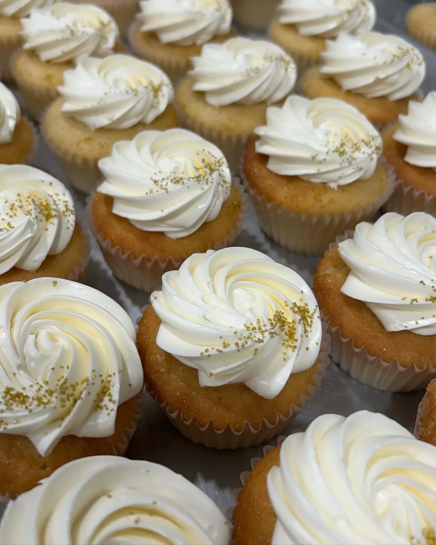 Close-up of vanilla cupcakes with white frosting and gold sprinkles