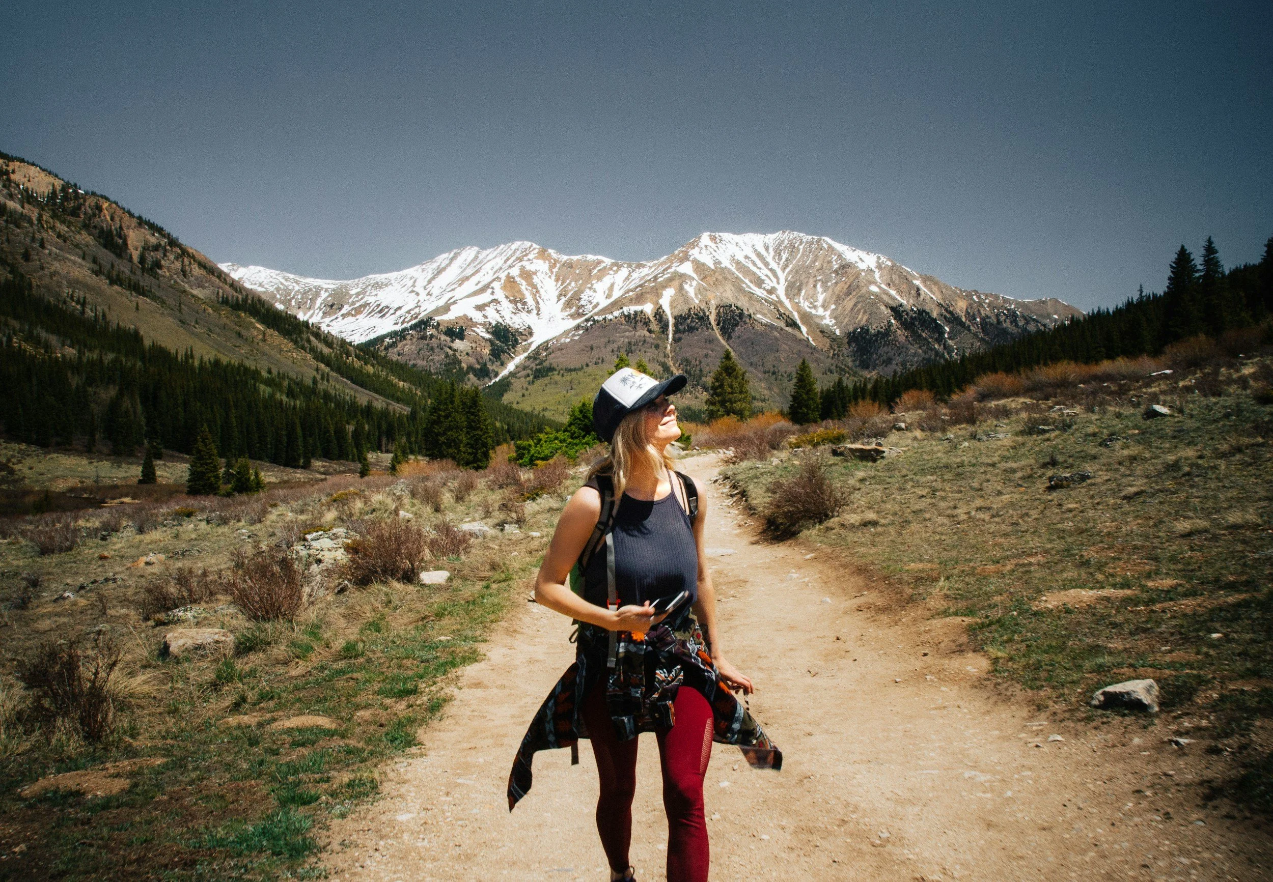 Woman hiking on a mountain trail with snow-capped peaks in the background.