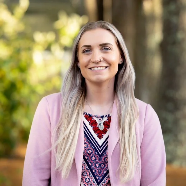Haley Clancy, a therapist at Eunoia Mental Health and Wellness in NJ, outdoors with long blonde hair, wearing a pink blazer and patterned top, smiling.