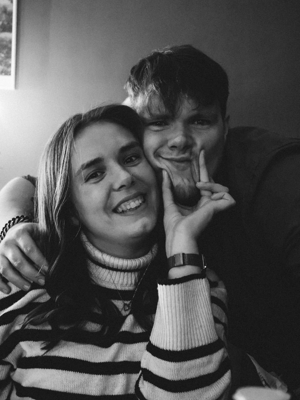 A young woman and a young man are smiling and making funny faces while posing for a photo together.