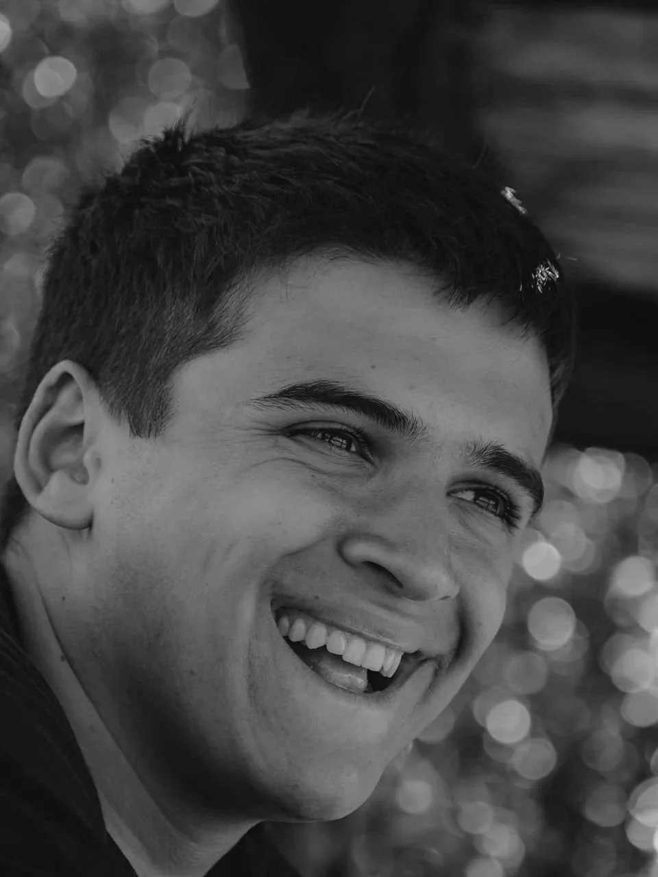 A young man with short dark hair smiling and showing his teeth, in black and white.
