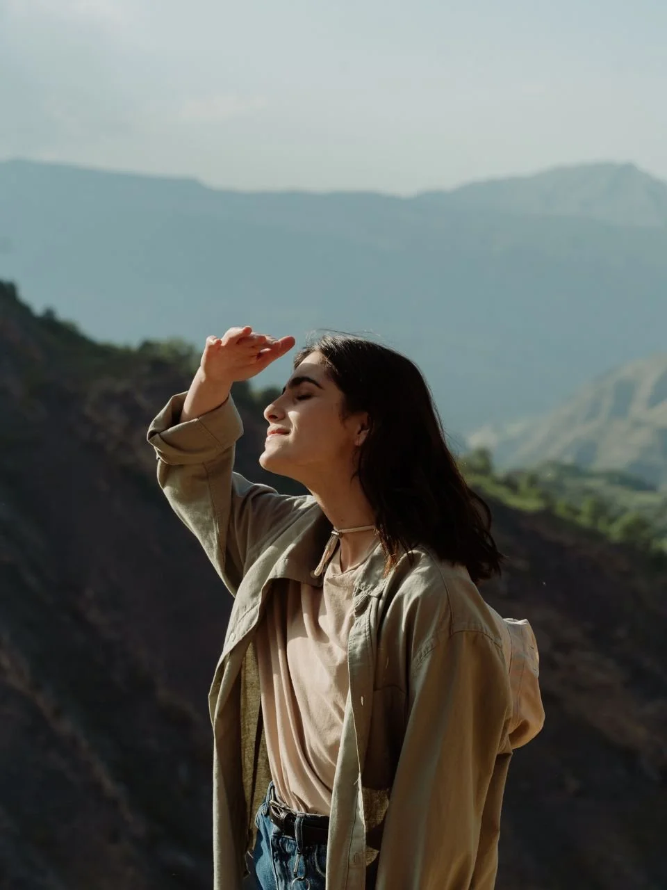 Young woman hiking in mountainous landscape, shielding eyes from the sun with her hand.