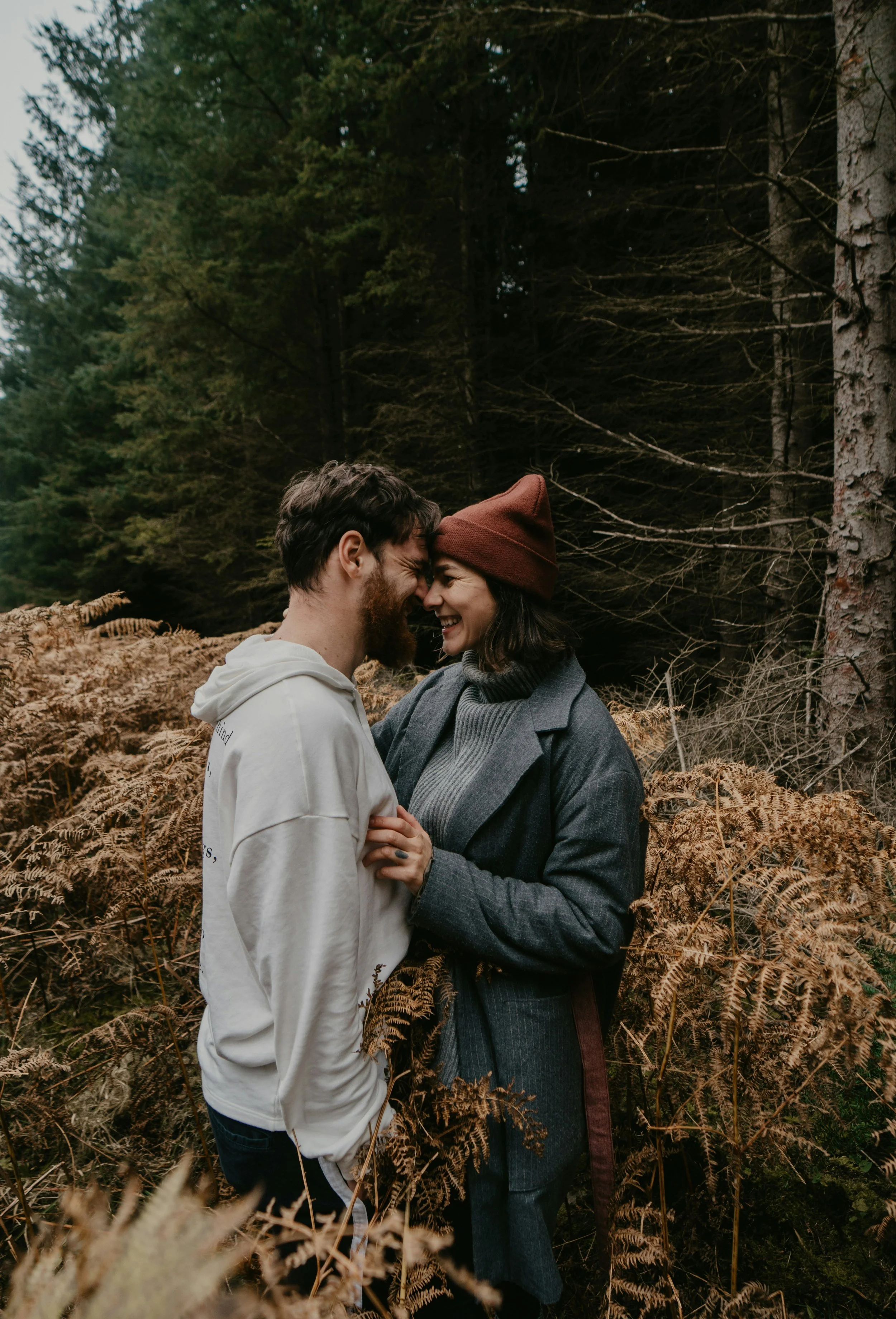 A couple sharing a close, joyful moment in a forest, with their foreheads touching and smiling.