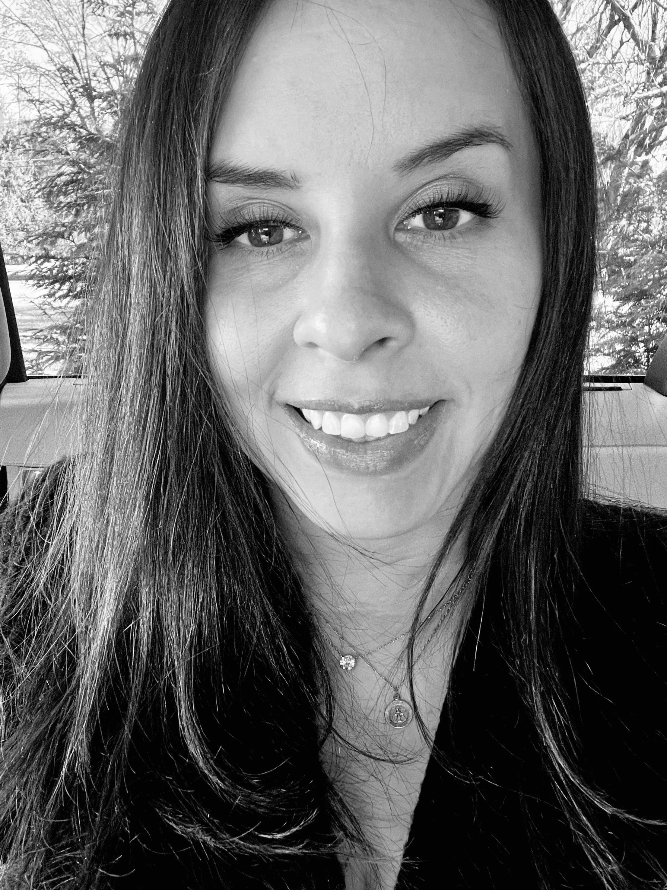 Close-up of Tierney, owner of Eunoia Mental Health and Wellness, with long dark hair, wearing a necklace, in monochrome photograph.
