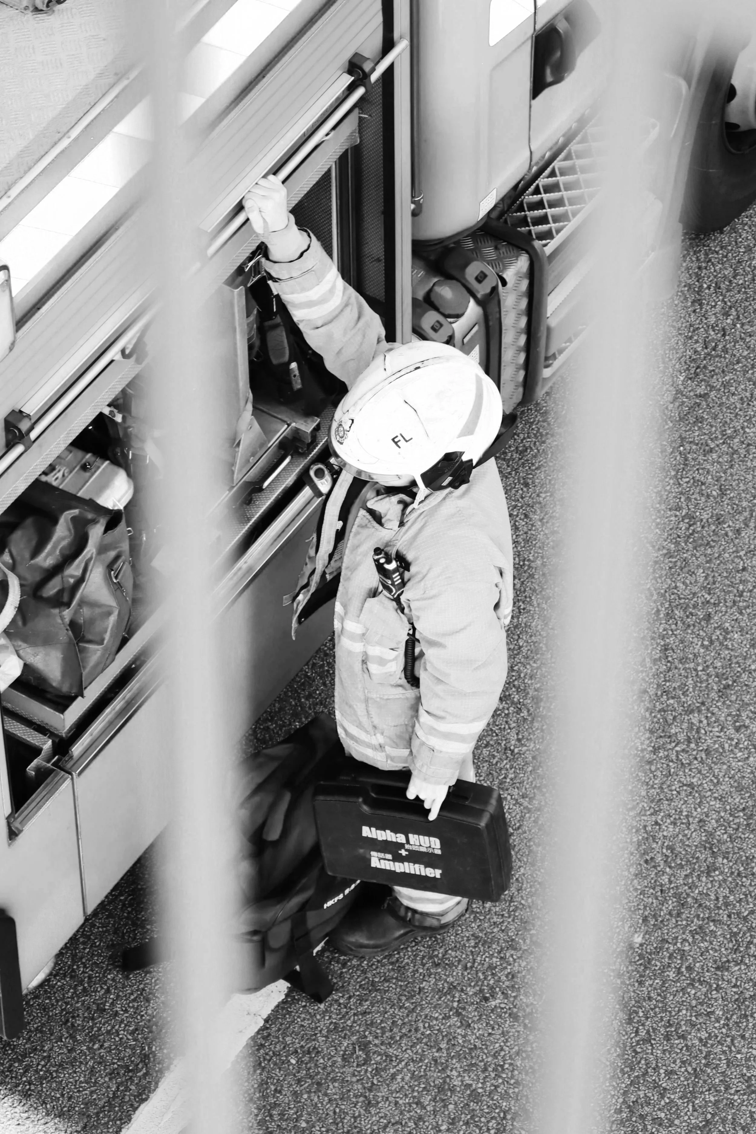 Firefighter in protective gear with helmet and gloves, working with equipment stored in a compartment, carrying a black case labeled ‘Alpha HUD + Amplifier’.