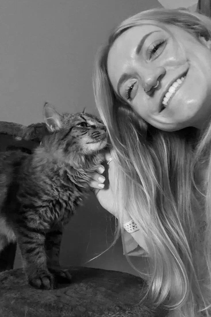Haley Clancy, therapist at Eunoia Mental Health and Wellness, with long hair, smiling with her eyes closed, holding a tabby cat close to her face, both appearing happy.