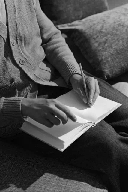 Person sitting on a couch writing in a notebook with a pen.