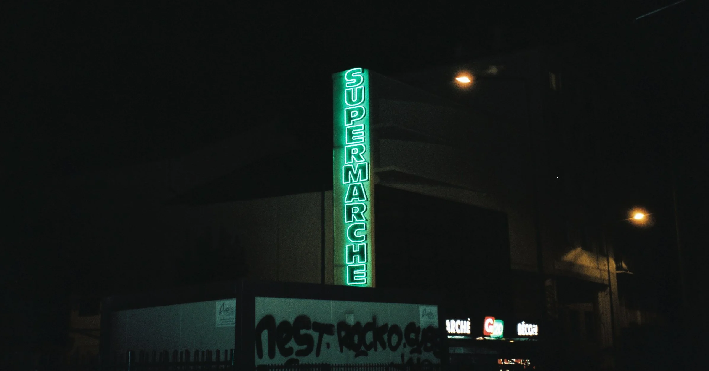 Panneau lumineux vert indiquant 'SUPER MARCHÉ' dans une zone urbaine la nuit.