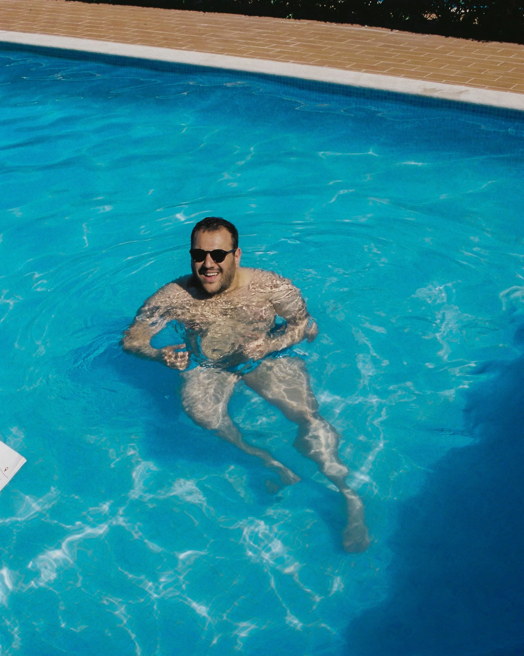 Un homme portant des lunettes de soleil nage dans une piscine avec un sourire.