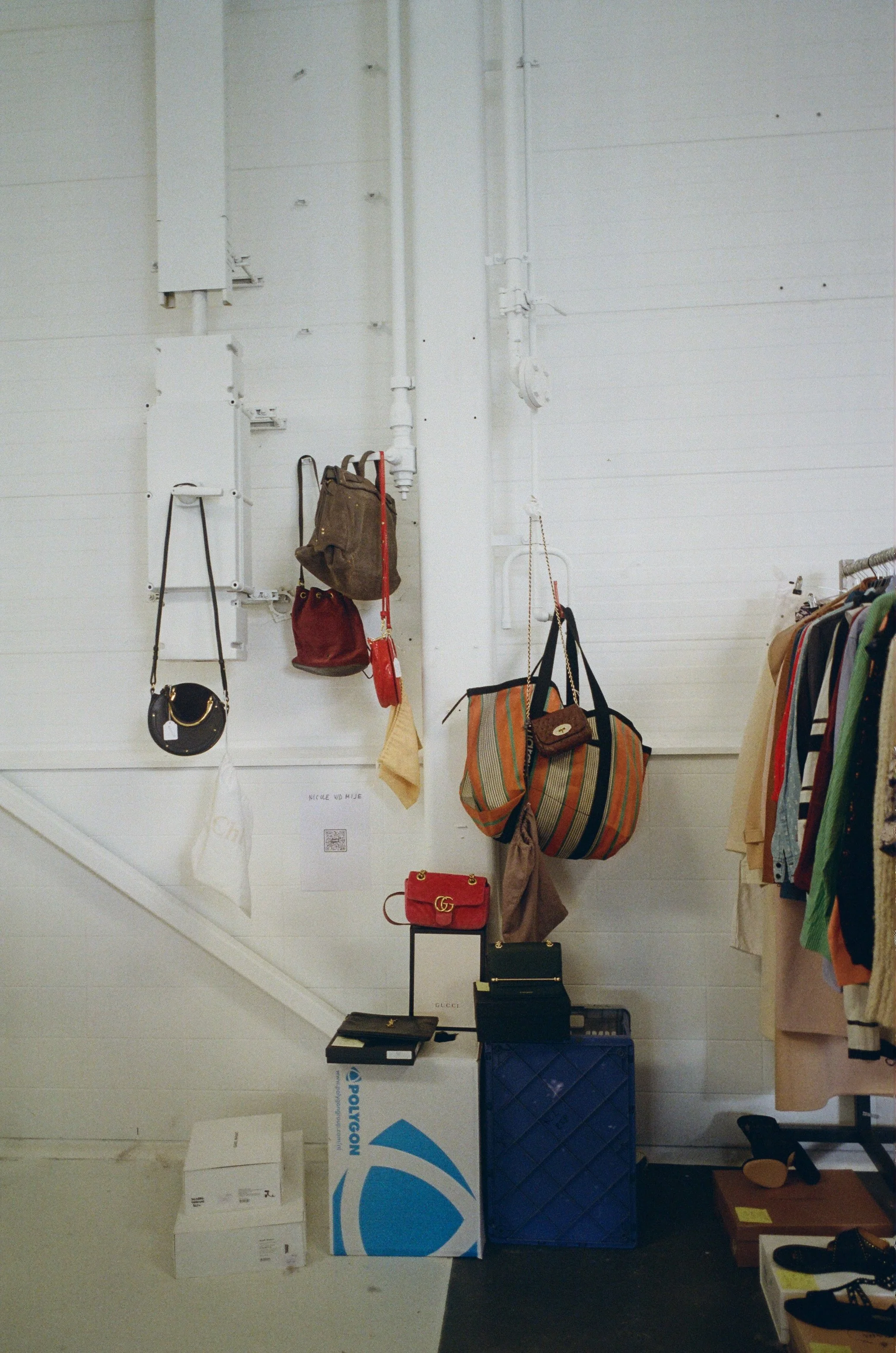 Vêtements et sacs à main affichés dans une boutique, avec quelques cartons au sol.