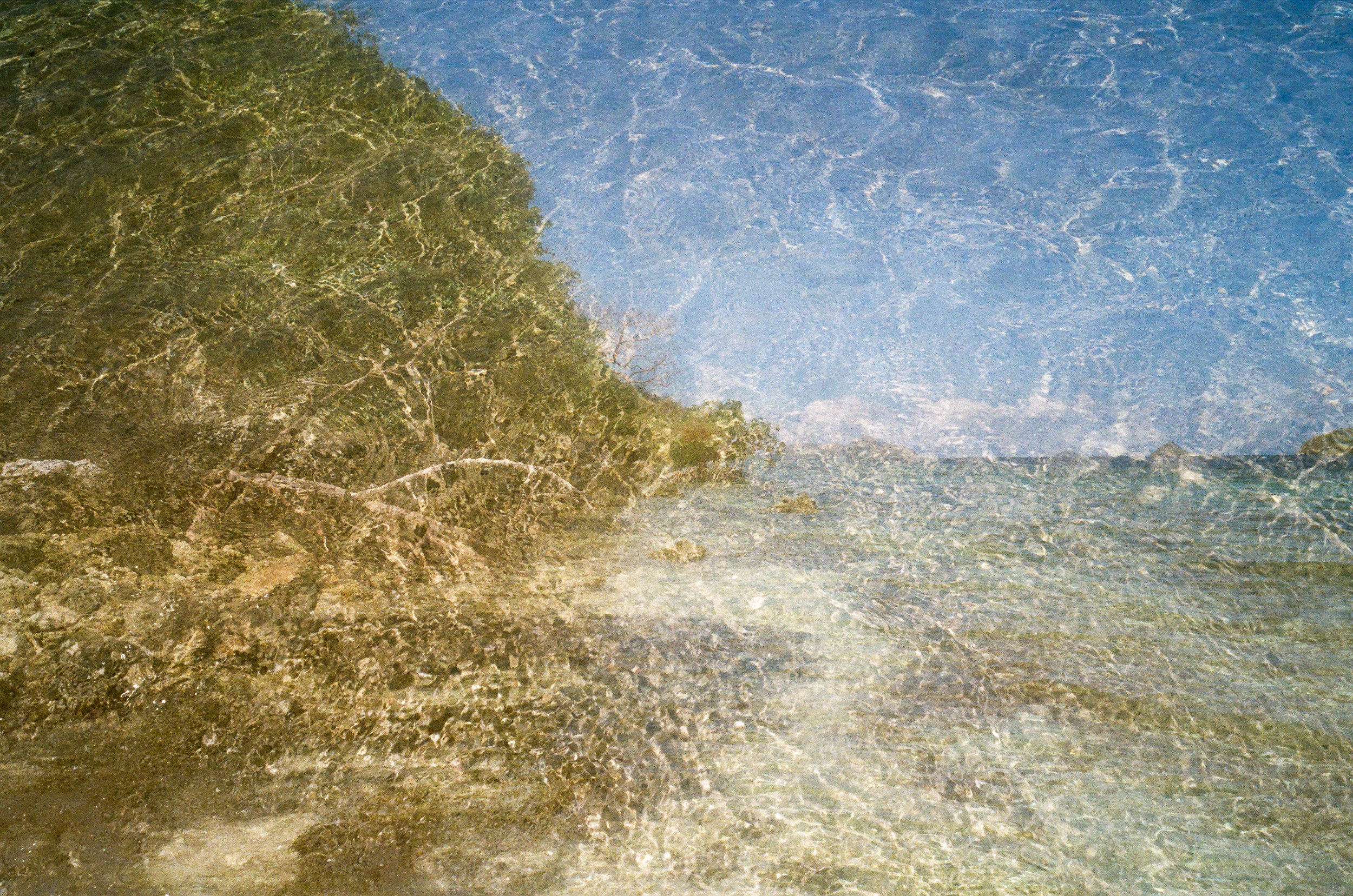 Paysage marin avec mer transparente, rochers et végétation côtière, ciel bleu