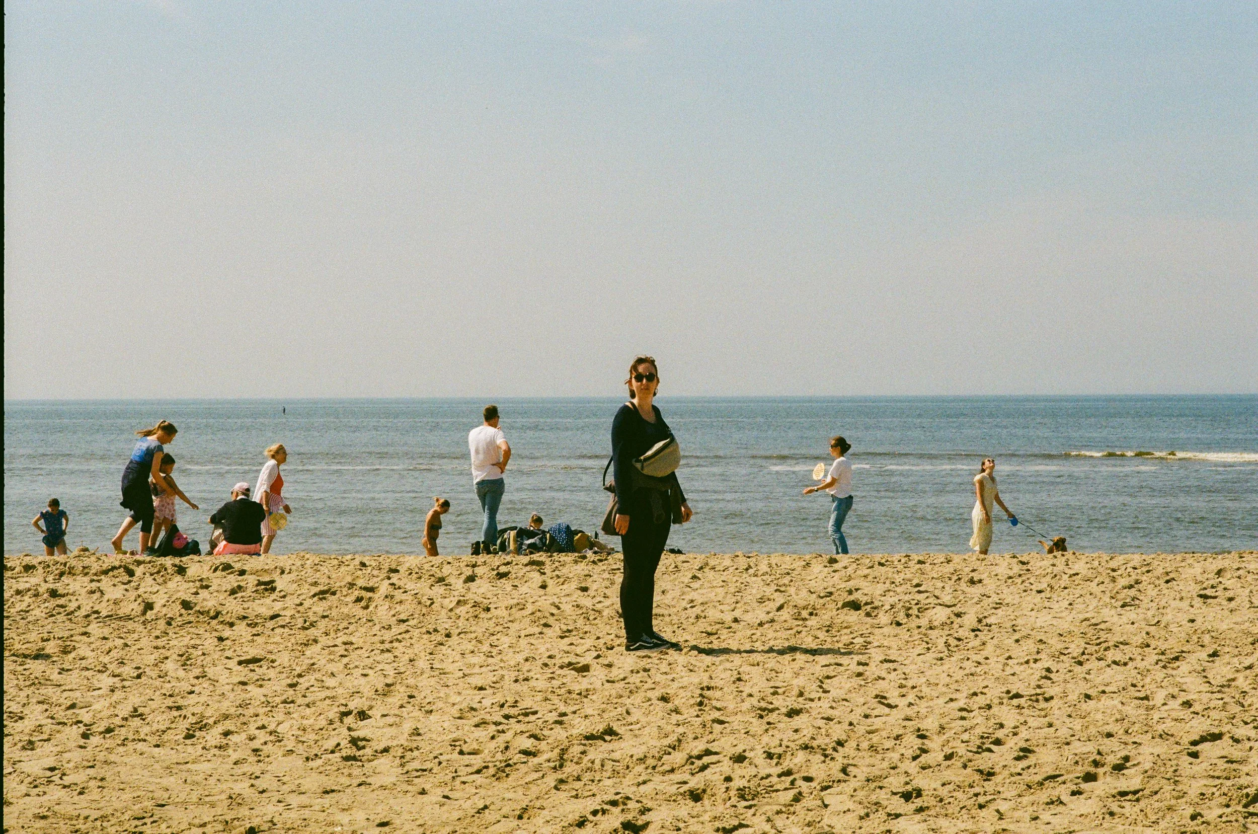 Personne debout sur la plage avec des enfants et d'autres personnes au bord de la mer, ciel clair.