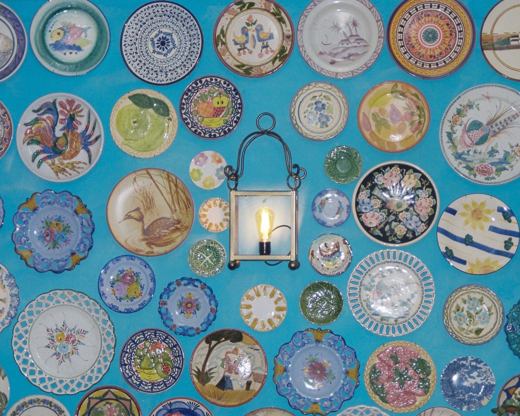 Collection de plusieurs assiettes colorées avec différents motifs, disposées sur un fond bleu, avec une lampe en forme de cadre lumineux au centre.