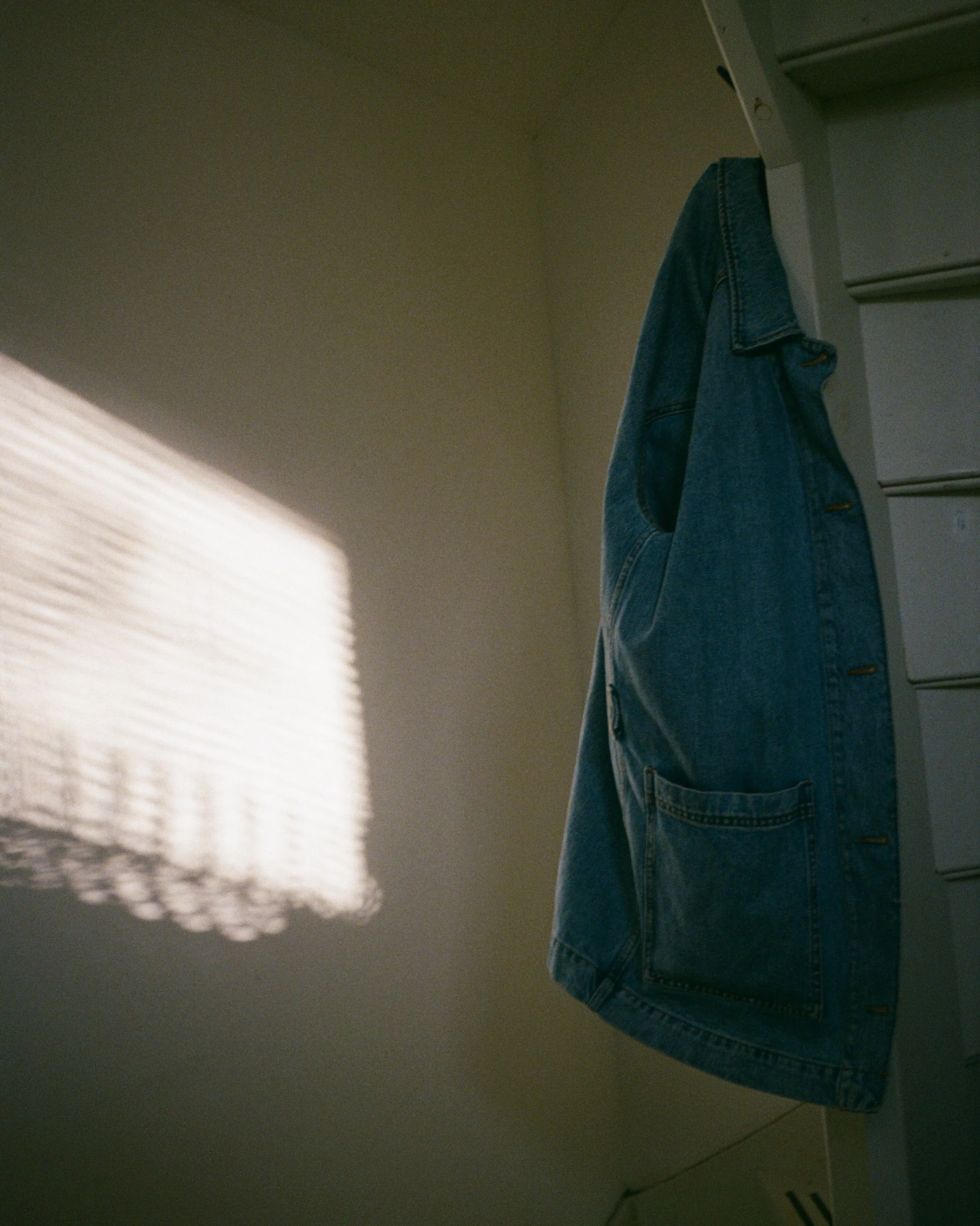 Une veste en jean suspendue sur une étagère blanche, avec une lumière douce sur le côté gauche.