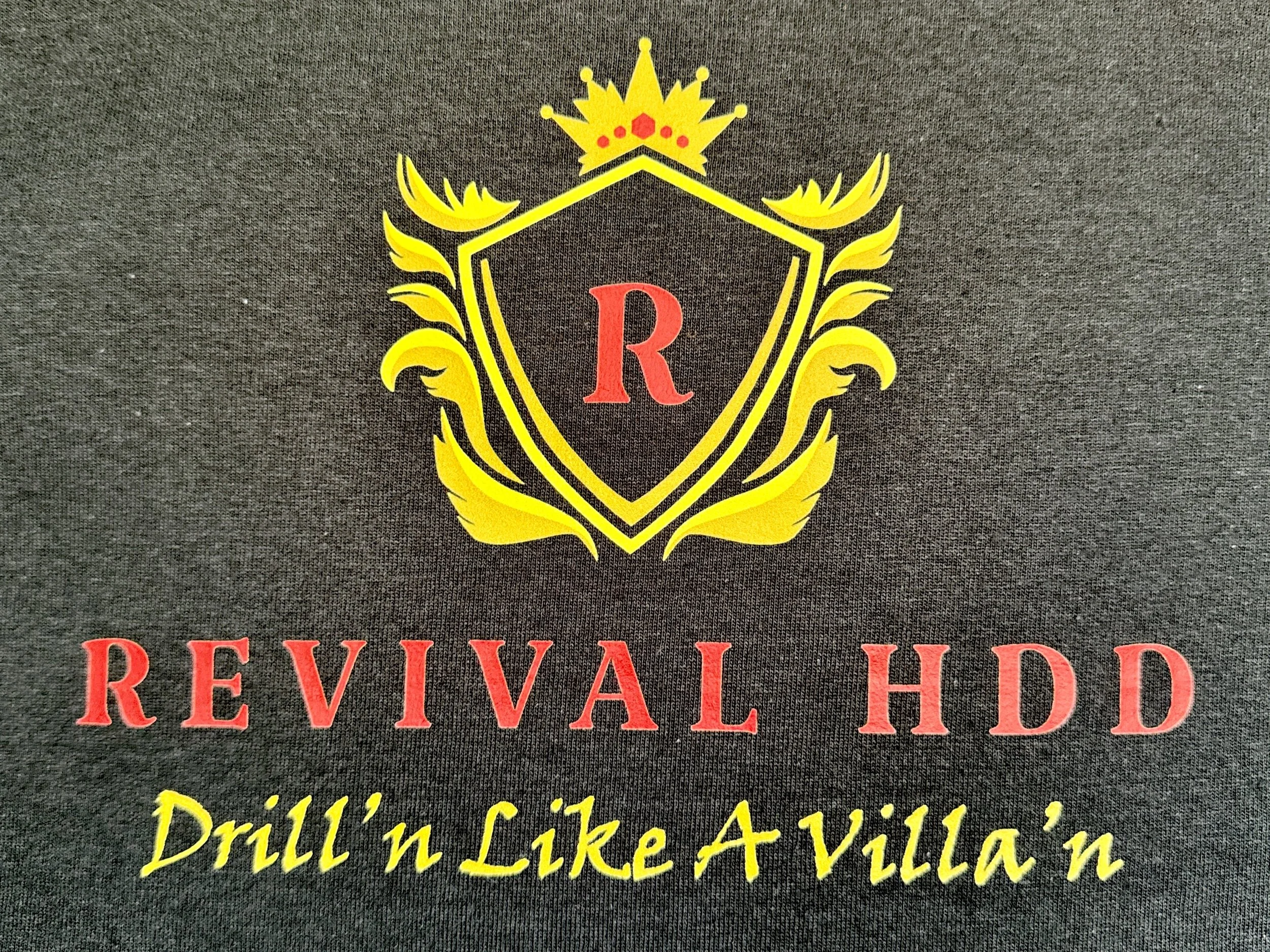 Black fabric with a yellow and red emblem featuring a shield, a crown, and the letter R. Below, red text reads 'REVIVAL HDD' and yellow text says 'Drill'n Like A Villa'n'.