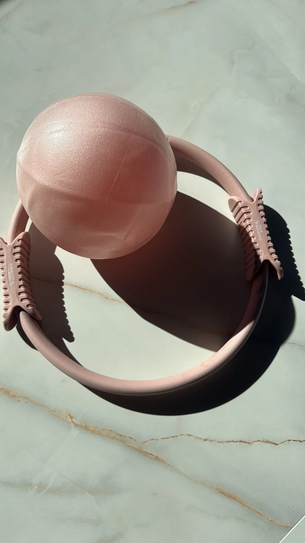A pink exercise ball resting on a pink headband with a light grey marble surface background.