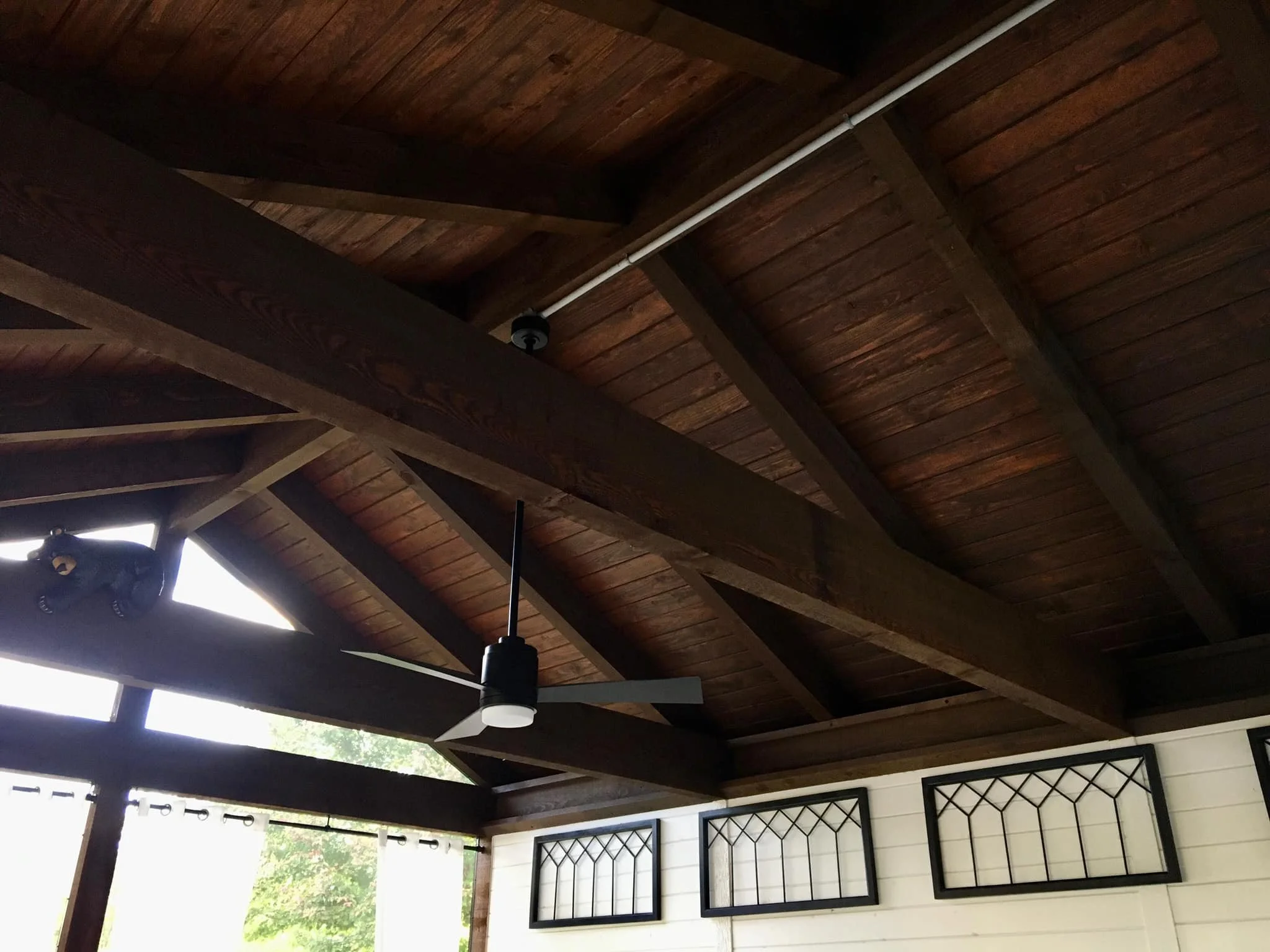 Wooden vaulted ceiling with a ceiling fan, ceiling light, and windows with curtains.