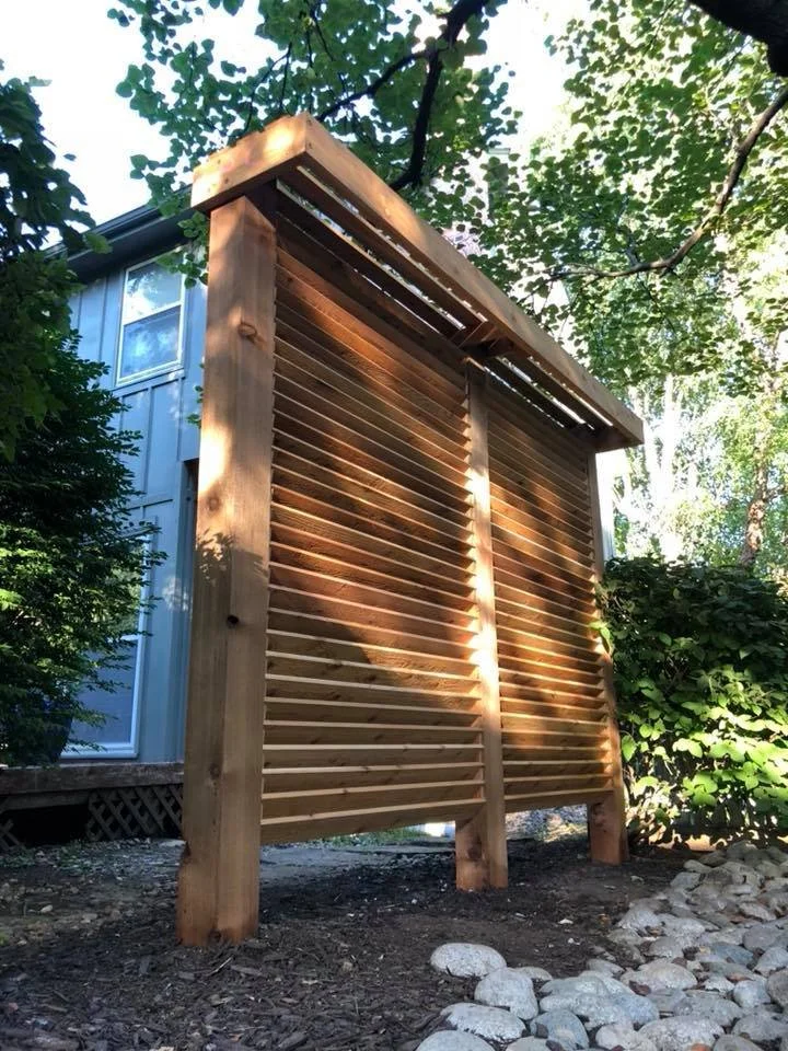 Wooden louvered privacy screen or fence with sunlight filtering through in a garden.