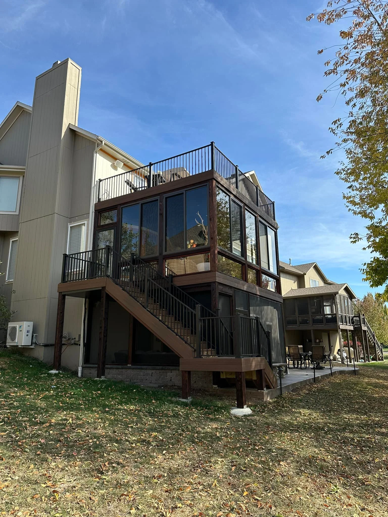 Multi-story house with a screened-in porch, outdoor staircase, and balcony, surrounded by leaf-covered ground and a blue sky with some clouds.