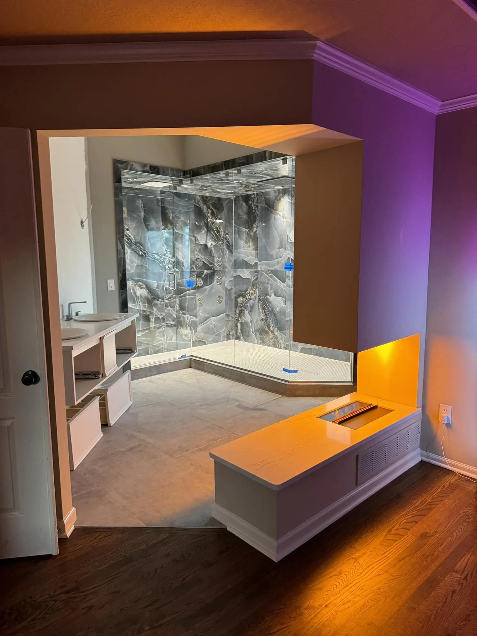 Bathroom with a glass-enclosed shower featuring gray and white marble tiles, double sinks, and colorful lighting on the walls and floor.