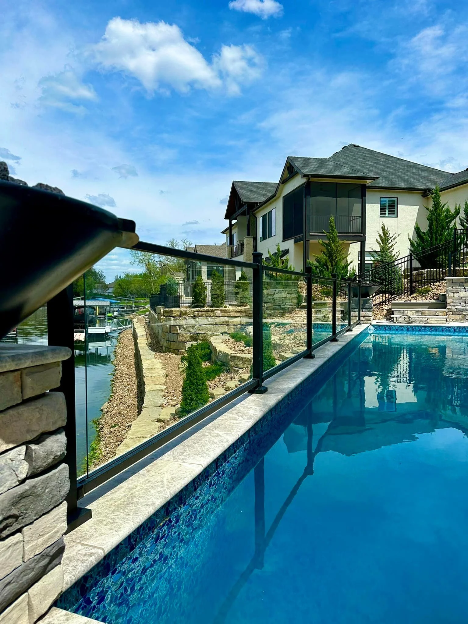 A backyard with a swimming pool, stone retaining walls, and a house with a screened porch on a sunny day.