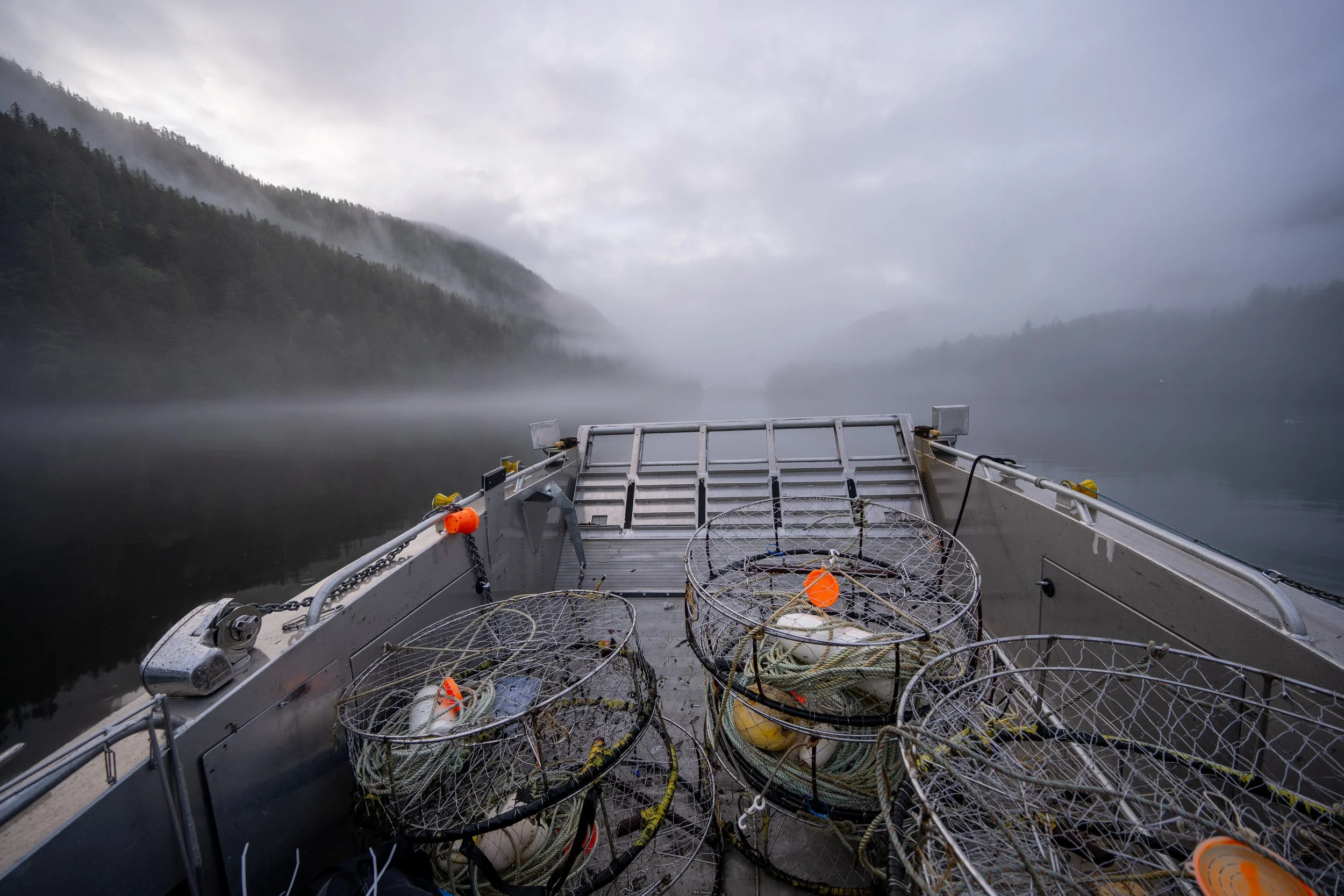 A boat on a calm, misty lake with fog-covered trees on mountains in the background.