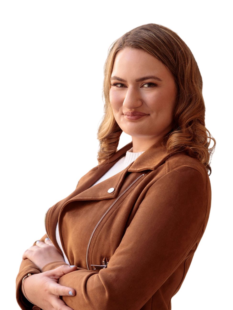 A young woman with light skin and wavy light brown hair smiling confidently, wearing a brown jacket and white shirt, with arms crossed.
