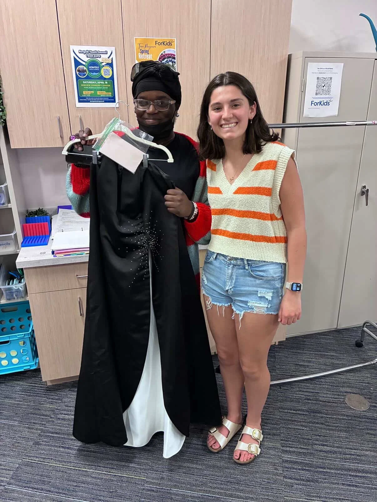2 women standing together. One, very happy, holding a dress that she just received from Let-Her Dress, the other, the Let-Her Dress founder, Mia Froehler, happy because she just donated a dress!