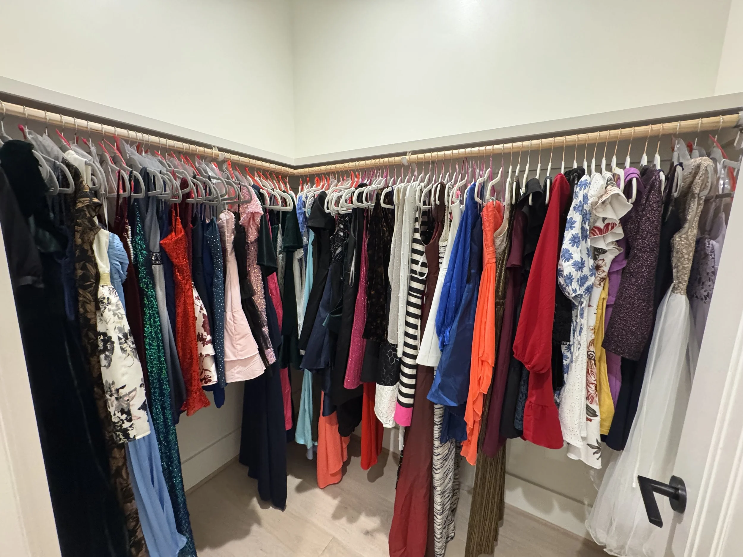 A walk-in closet with a shelf of hanging dresses, skirts, and tops in various colors and styles.