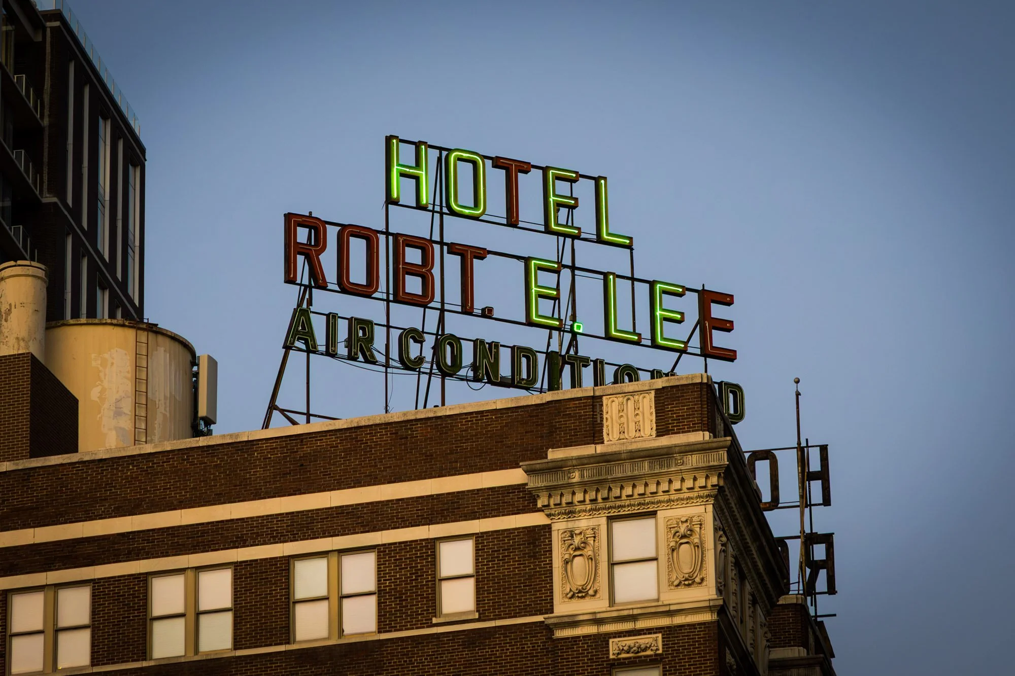 Neon sign on top of a brick building reading 'Hotel E. Lee', 'Roth', and 'Air Conditioning' against a blue sky.