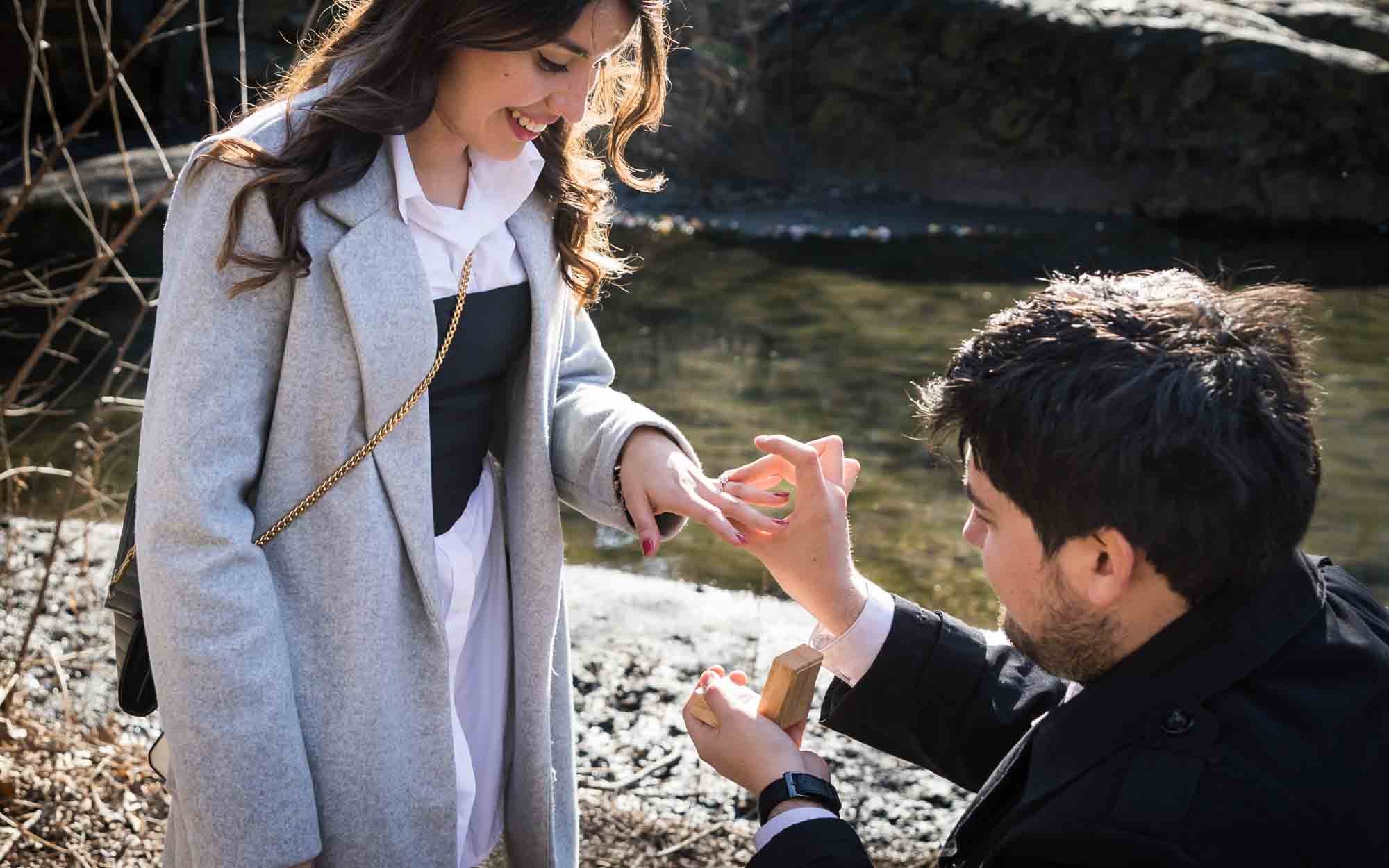 Man kneeling on ground putting engagement ring on woman's finger as photographed by San Antonio surprise proposal photographer, Kelly Williams