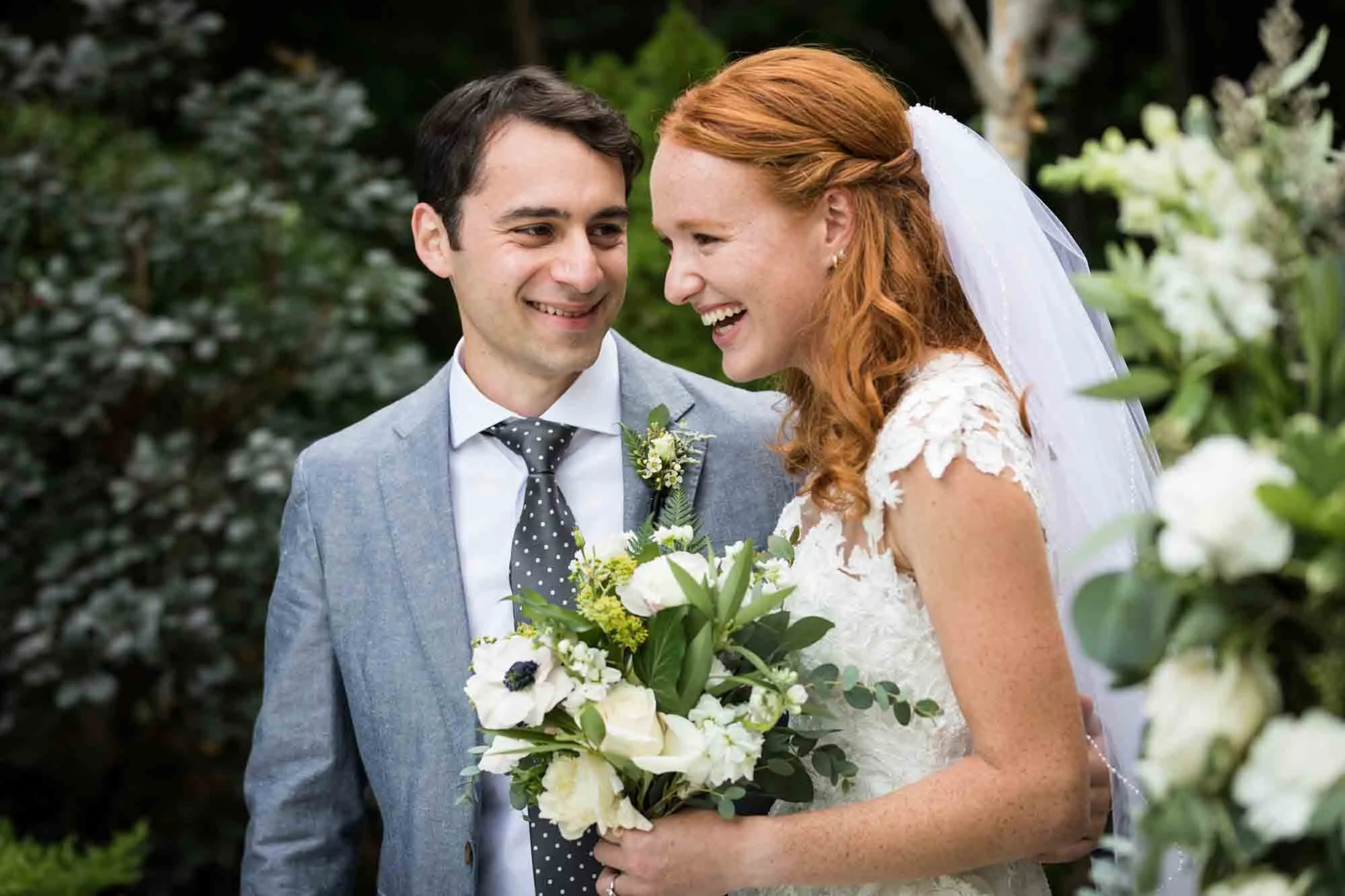 Bride holding flower bouquet laughing with groom in front of bush by San Antonio wedding photographer, Kelly Williams